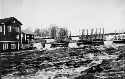 19xx Råneå Norrforsen nedanför bron.jpg - Vy över kraftverket med dammluckorna öppna i strid vårflod, kraftverket är den låga byggnaden den höga byggnaden bakom är kvarnen och längre bort kvarnstugan.